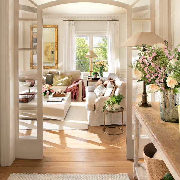 Recibidor clásico con salón al fondo, puerta con arco de cristal, sofás blancos y flores